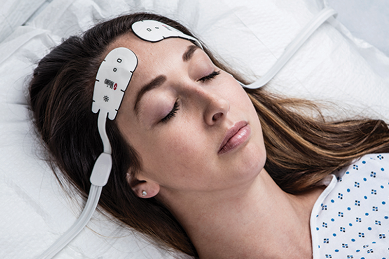 Patiente à la peau foncée dans un lit d'hôpital surveillée par un appareil Masimo Root.